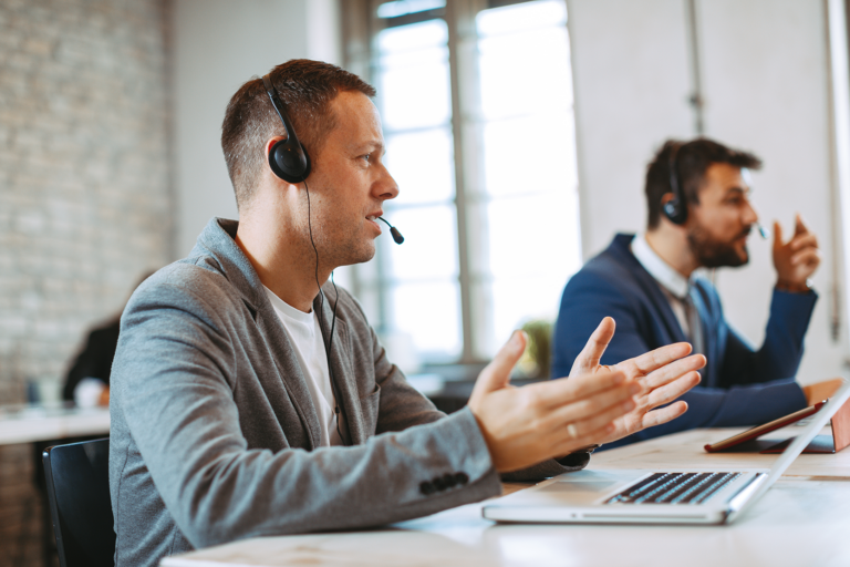 a man at his computer talking with his hands while wearing a headset