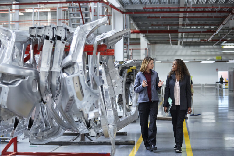 2 women talking in a car factory