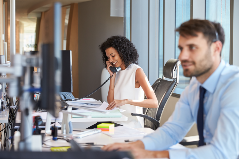 woman sitting at desk looking at papers and on phone