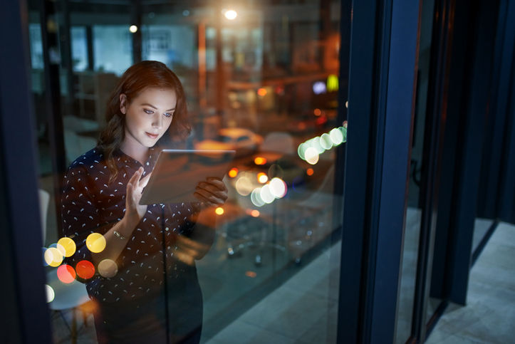 Woman on tablet in dark, view through business window