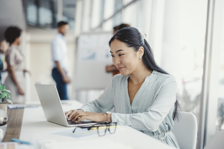 Woman working on laptop. Businesswoman busy working on laptop computer at office with colleagues in the background.